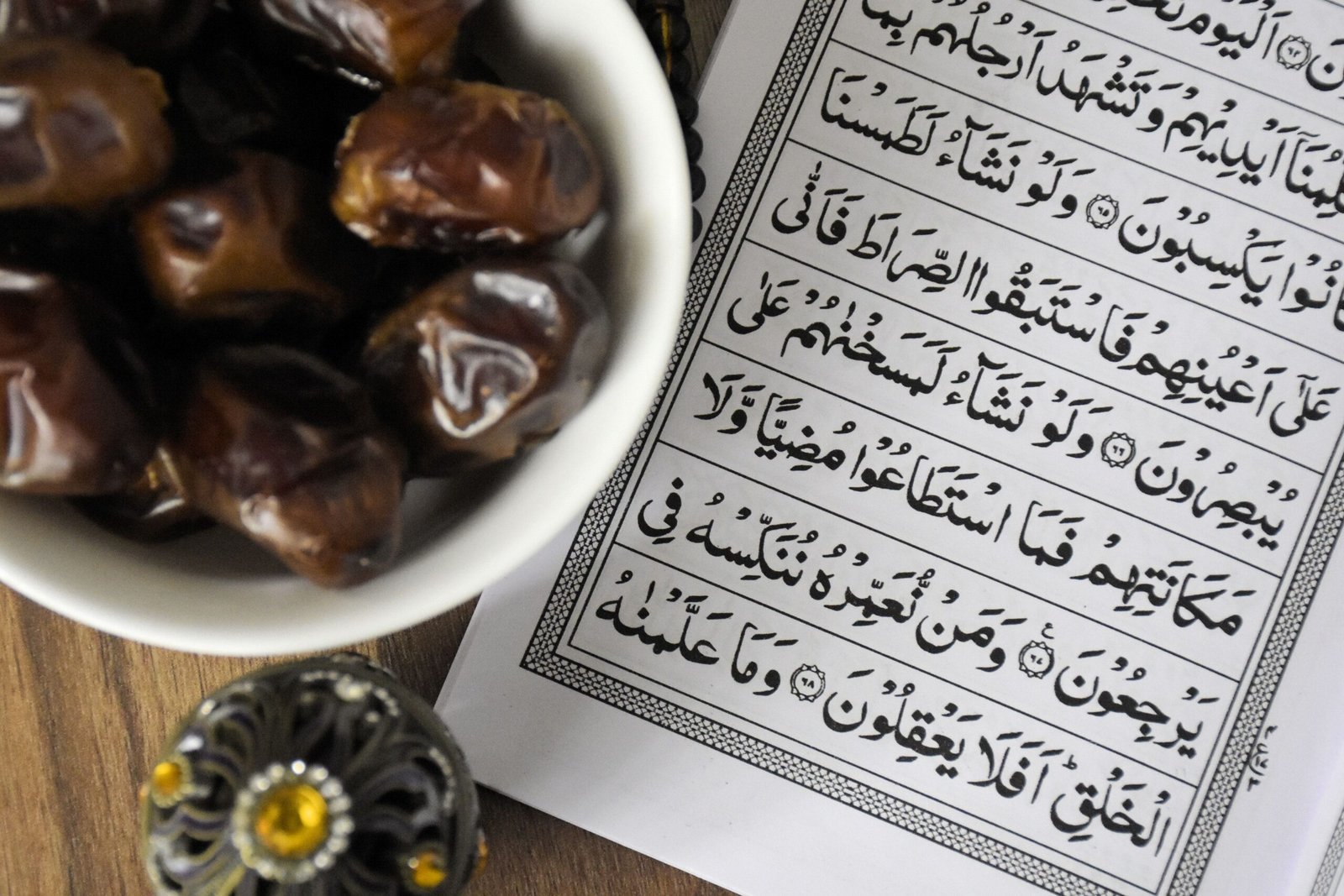 طفل يمسك بكتاب بجانب سبحة على طاولة خشبية